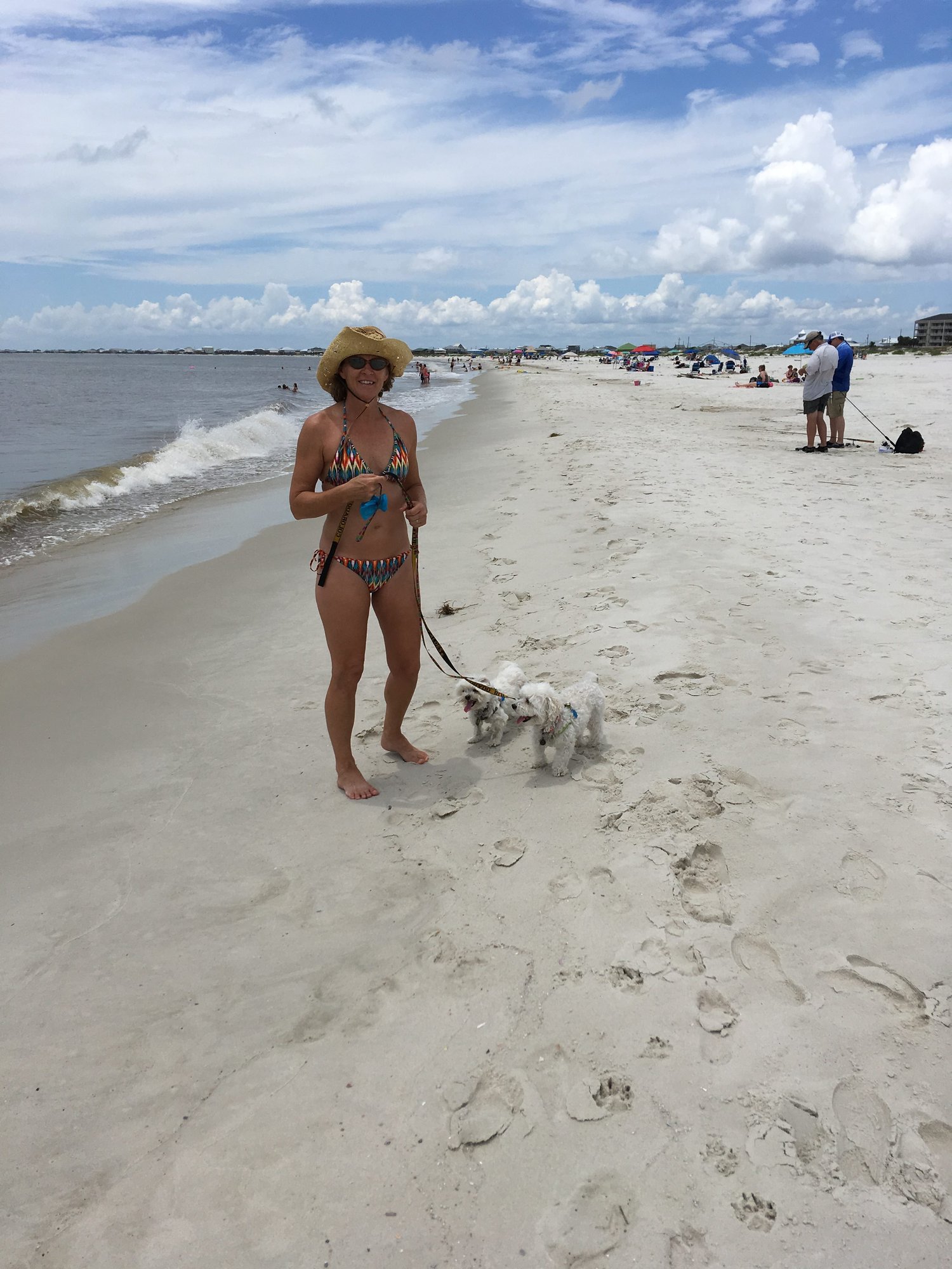 Deb in a bikini on the beach with two dogs on leash